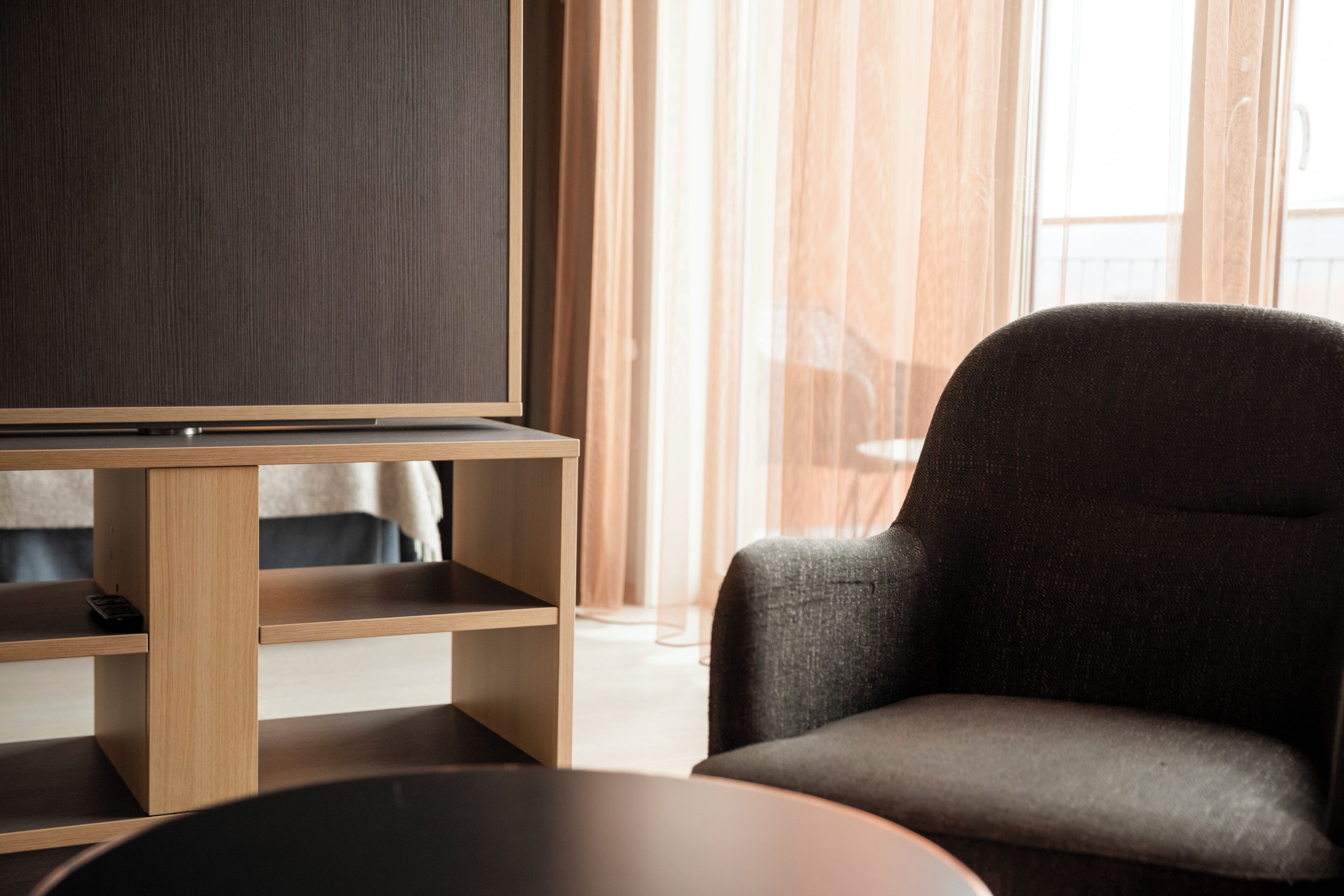 A modern living room with a flat-screen TV on a wooden stand, a dark armchair, and a round coffee table.