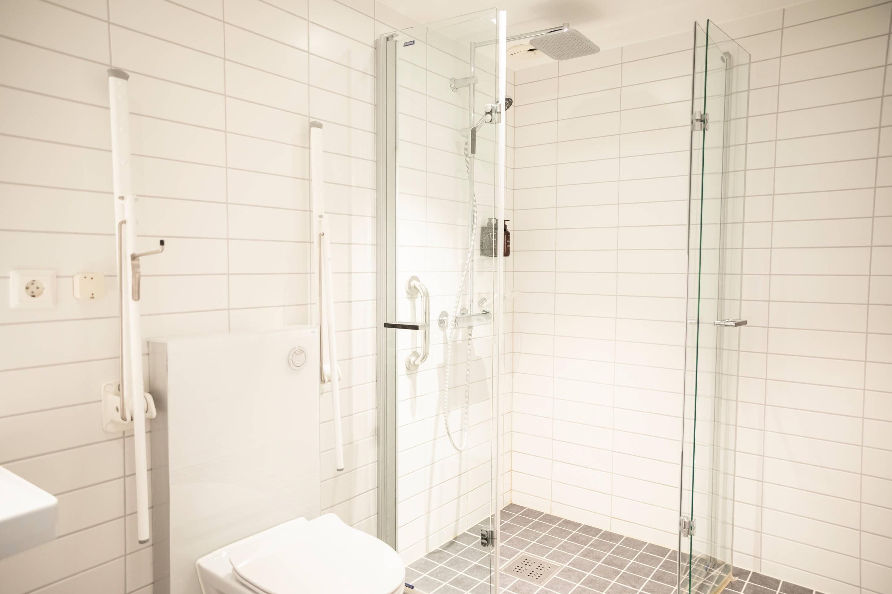 Une salle de bain moderne avec une douche à parois de verre, des toilettes blanches et un sol carrelé.
