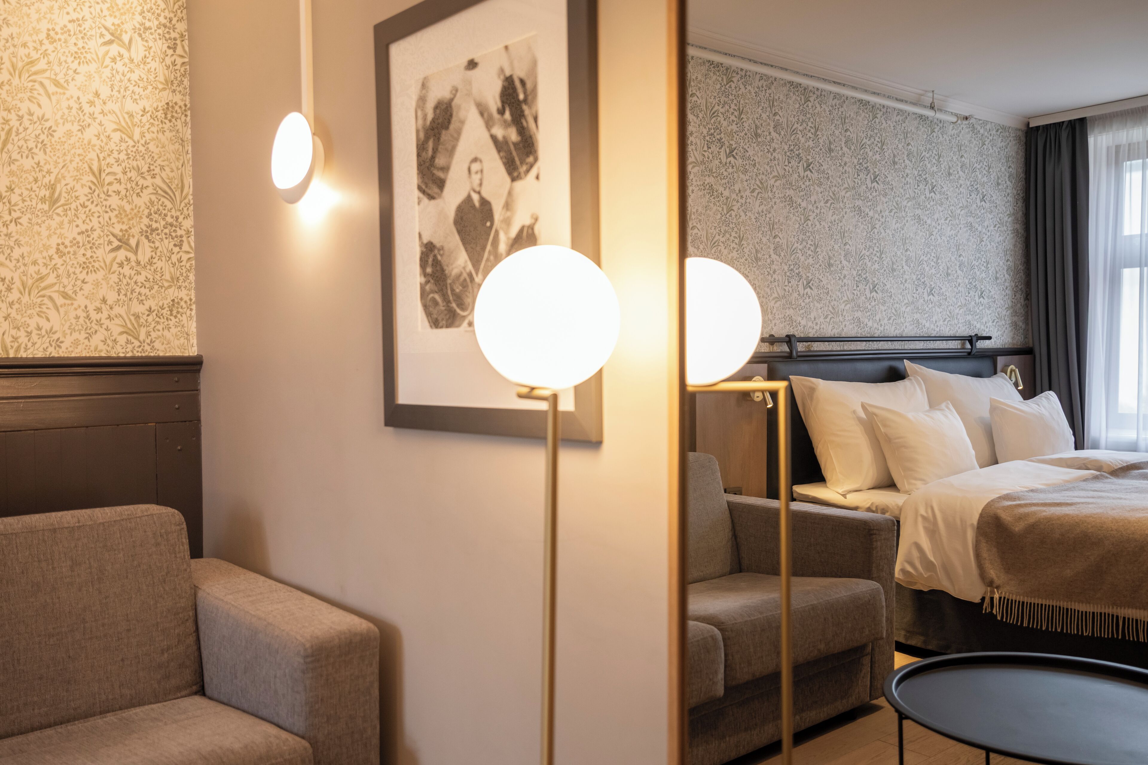 A hotel room with a bed, a sofa, a small round table, and a framed photograph on the wall.
