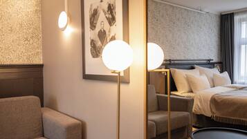 A hotel room with a bed, a sofa, a small round table, and a framed photograph on the wall.