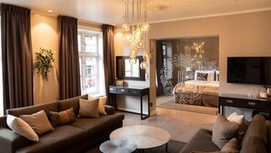 A modern living room with a sofa, coffee table, and a TV. There is a desk with a mirror and a chandelier.