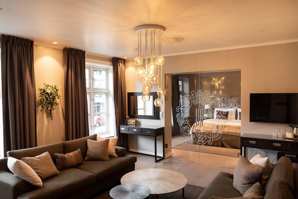 A modern living room with a sofa, coffee table, and a TV. There is a desk with a mirror and a chandelier.
