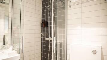 A modern bathroom with a glass shower enclosure, a white sink, and a tiled wall.