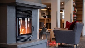 A modern fireplace with a metal front, a grey wall, and a sofa with red cushions in the background.