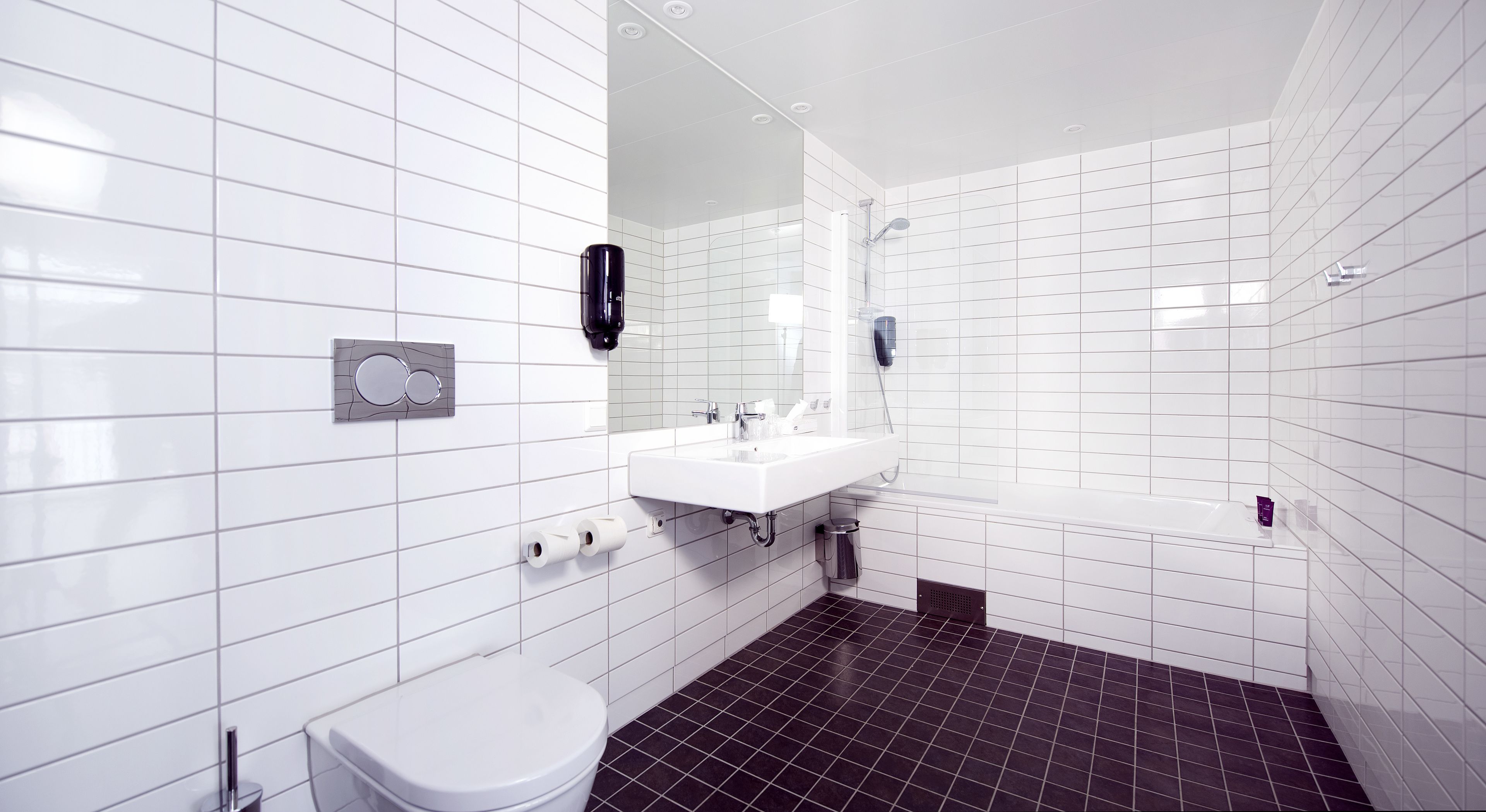 A modern bathroom with white tiles, a white sink, a toilet, and a shower.
