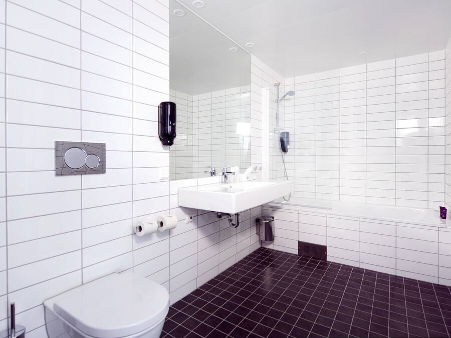 A modern bathroom with white tiles, a white sink, a toilet, and a shower.