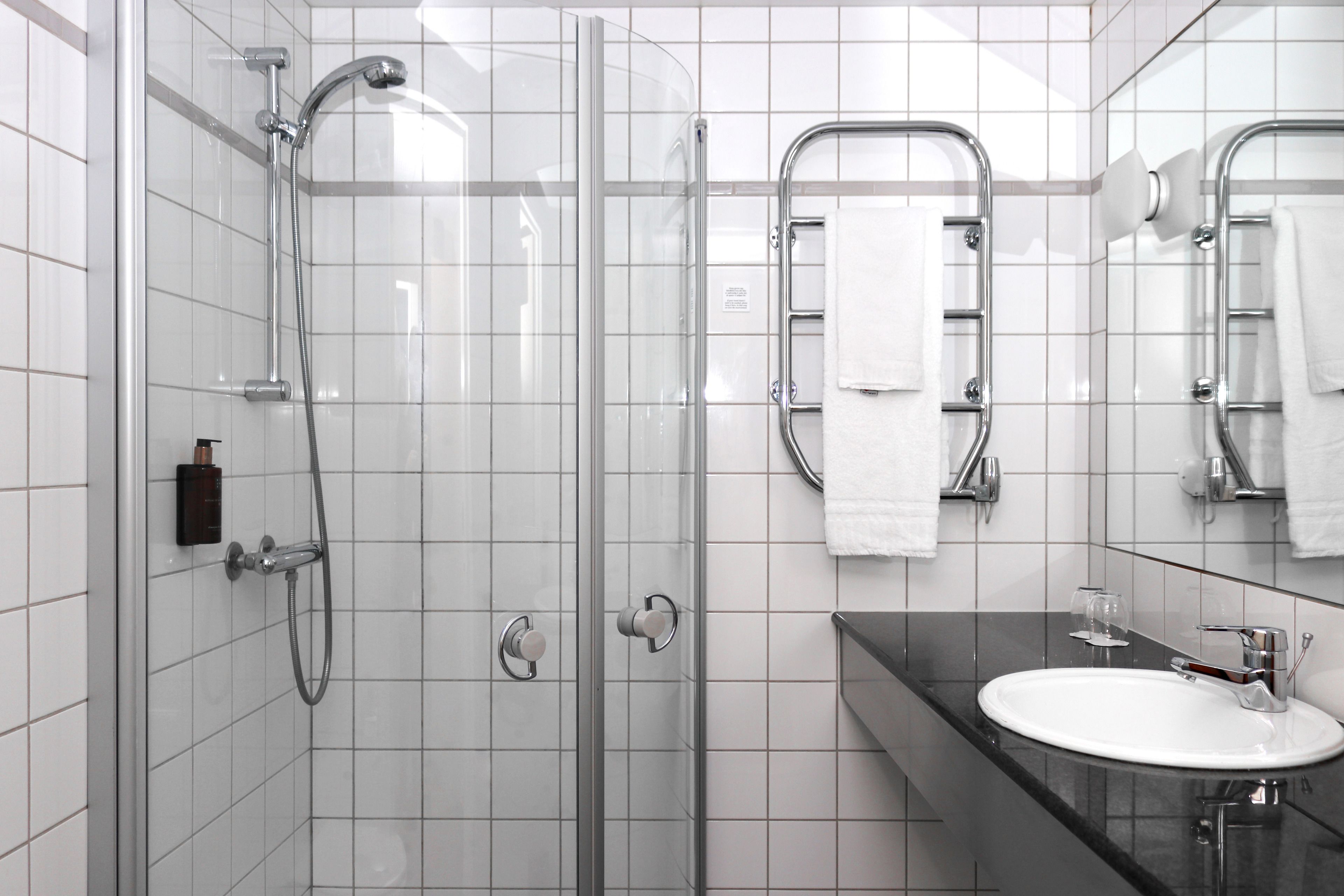 Une salle de bain moderne avec une douche en verre, un lavabo blanc et un miroir doté d’un porte-serviettes.