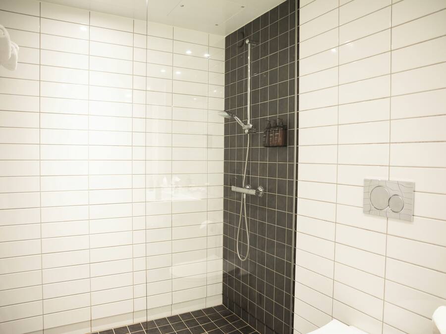 A bathroom with white and black tiles, a shower with a handheld showerhead, and a towel rack.