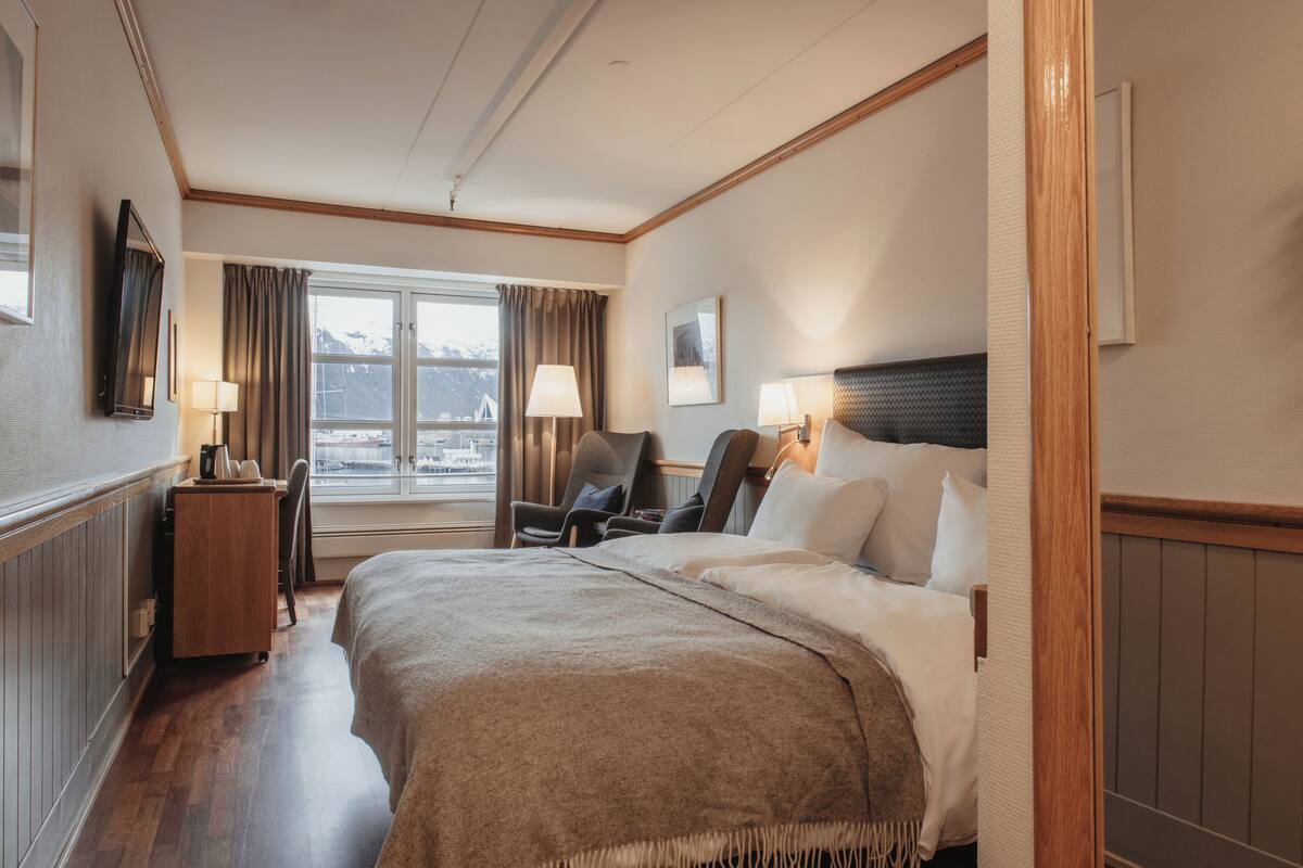 Une chambre d’hôtel avec un grand lit, deux tables de chevet, une chaise, une fenêtre avec des rideaux et une vue sur les montagnes.
