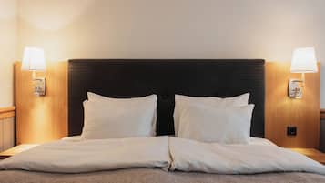 Un lit bien fait, avec du linge de lit blanc, une tête de lit sombre et deux lampes fixées au mur, une de chaque côté.