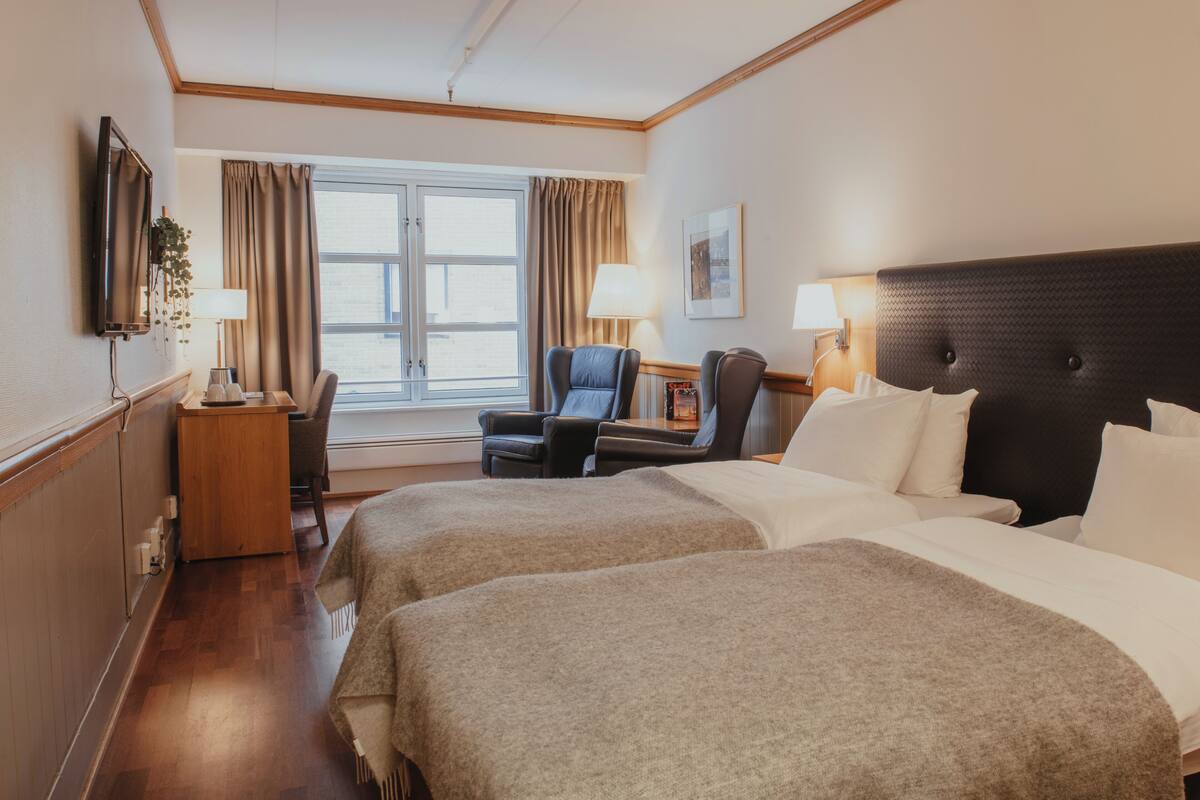 Une chambre d’hôtel avec deux lits, un bureau, une chaise, une télévision et une fenêtre avec des rideaux.