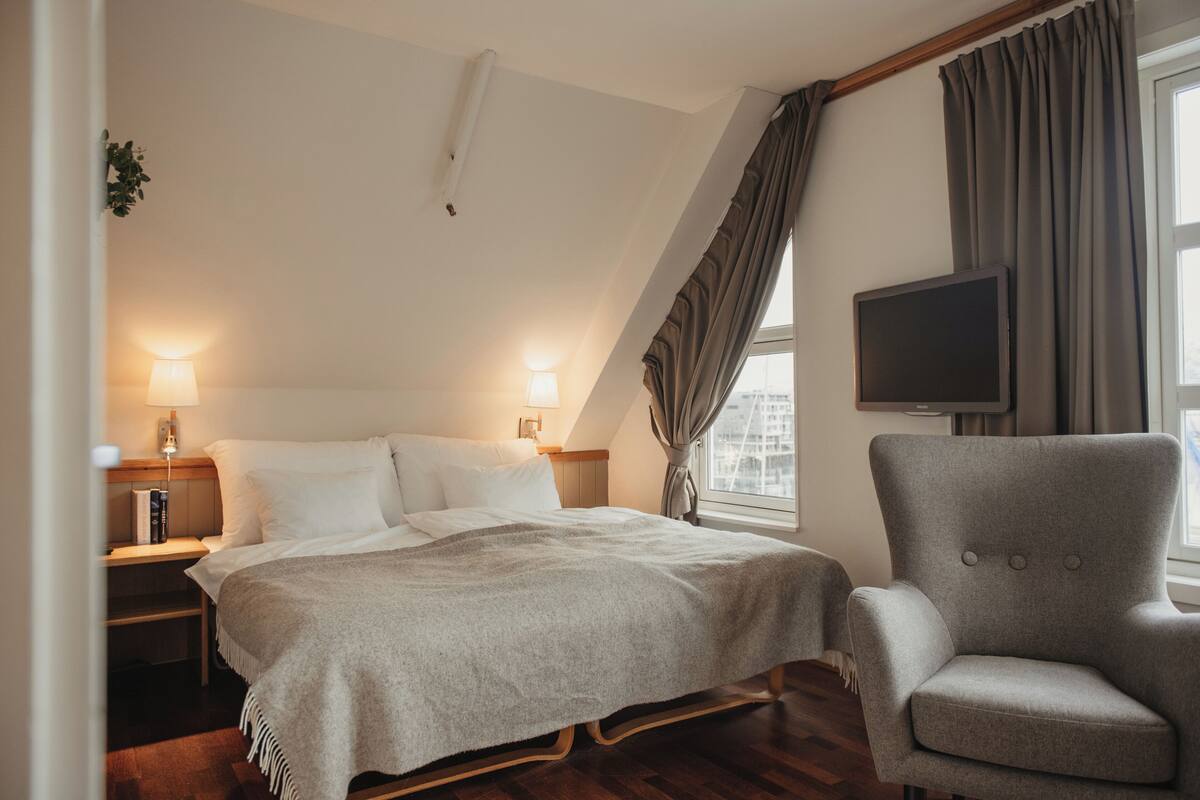 Une chambre d’hôtel avec un lit, des tables de chevet, une chaise, une télévision et une fenêtre avec des rideaux.