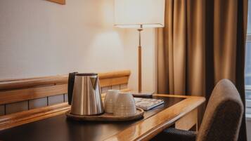 Une chambre d’hôtel avec une table en bois, une lampe, une bouilloire et deux tasses.