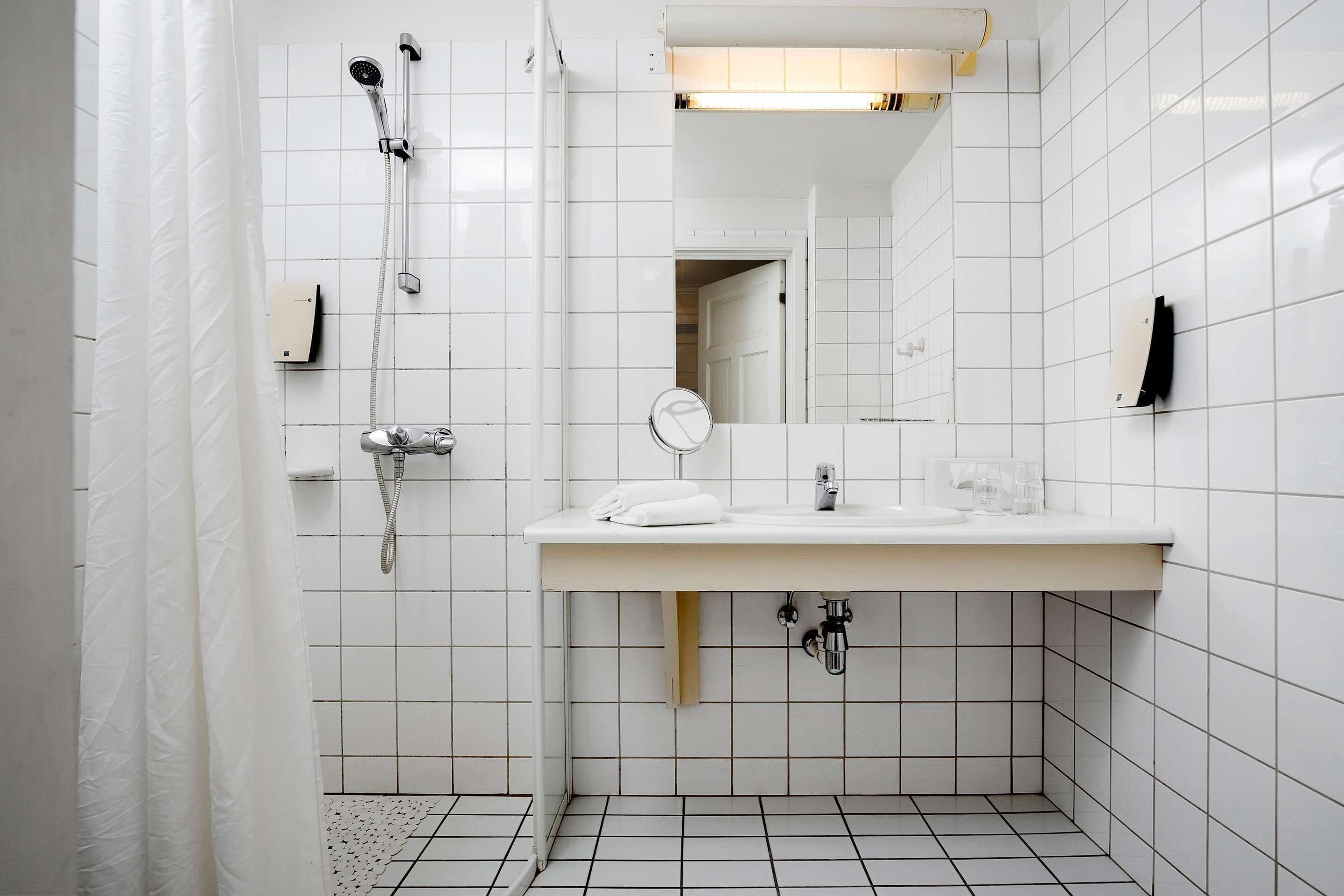 A modern bathroom with white tiles, a white sink, a mirror, and a shower with a handheld showerhead.
