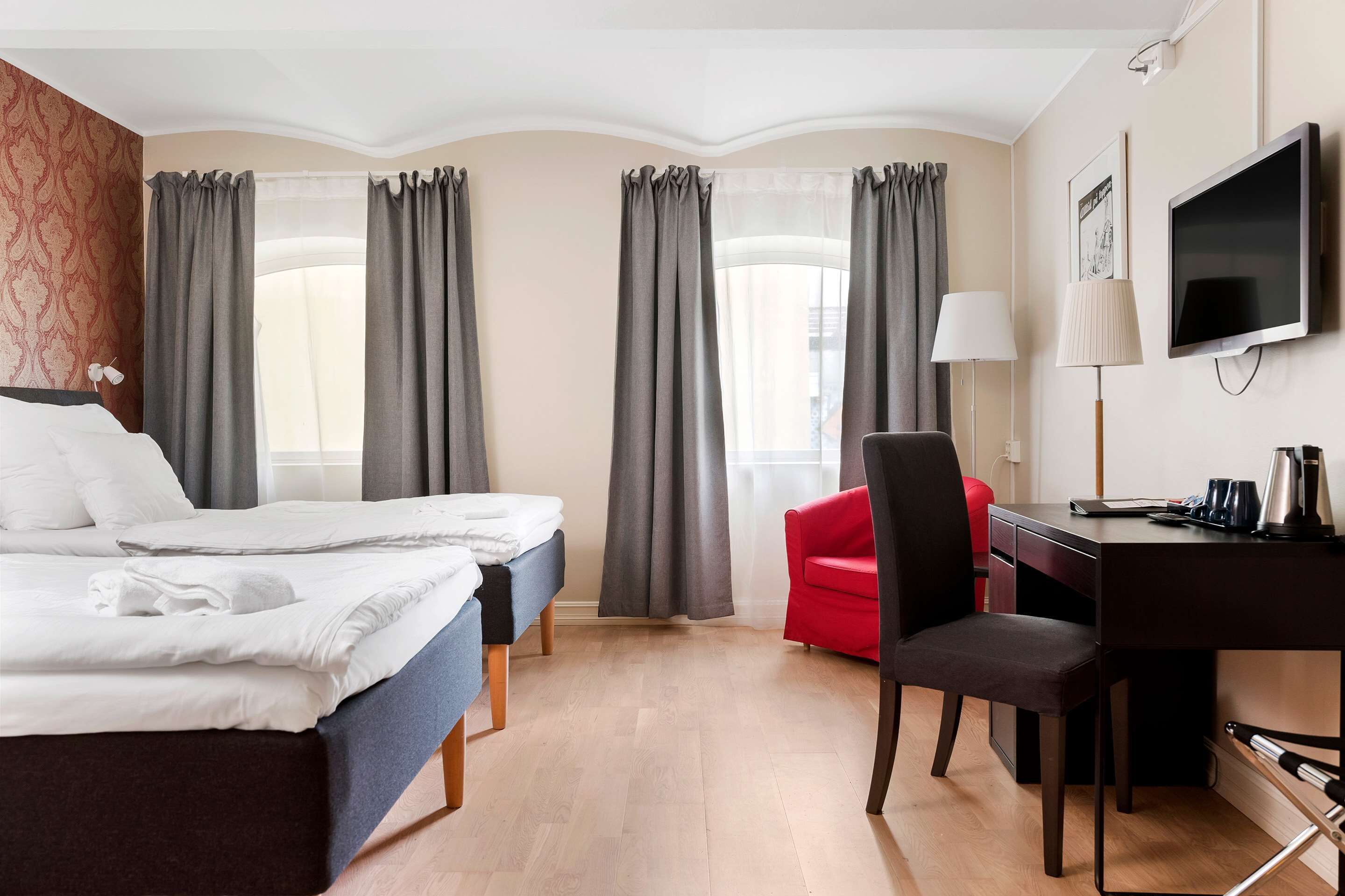 Een hotelkamer met twee bedden, een bureau, een stoel, een televisie en gordijnen.