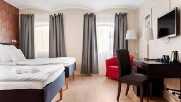 A hotel room with two beds, a desk, a chair, a TV, and curtains.