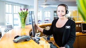 A reception desk with a computer, a cash register, and a vase of flowers. - Best Western Plus Hotel Bakeriet (Trondheim)