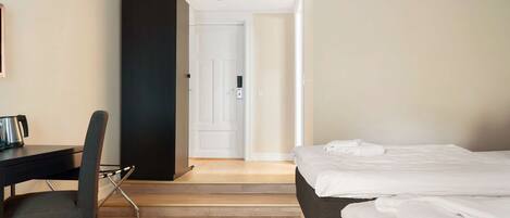 Quarto de hotel com uma cama, uma escrivaninha, uma cadeira e uma porta que dá para outro quarto.
