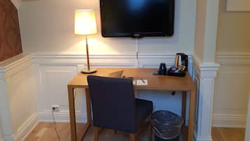 A hotel room with a bed, a desk with a chair, a television, a lamp, and a trash bin.