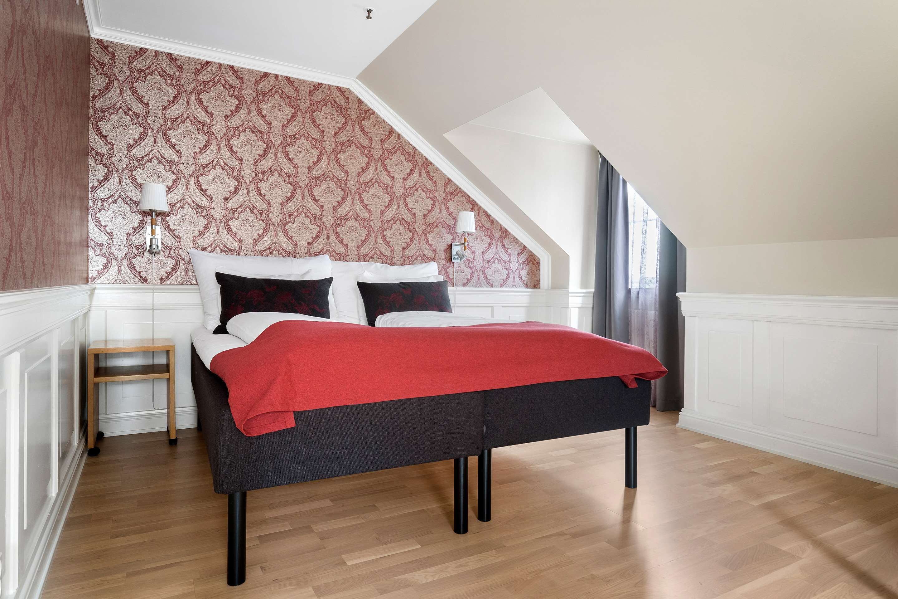 A bedroom with a bed, a nightstand, a lamp, and a window with curtains.