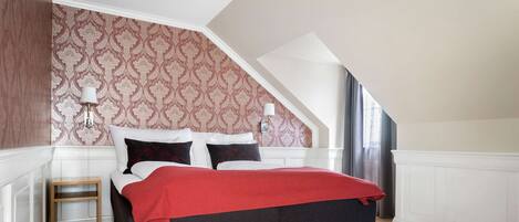 A bedroom with a bed, a nightstand, a lamp, and a window with curtains.