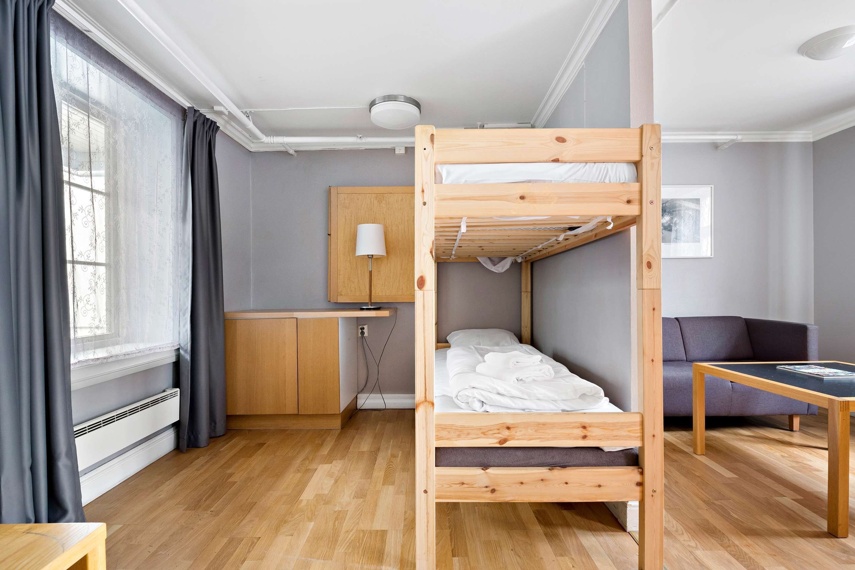 A bunk bed room with a desk, a sofa, and a window with curtains.