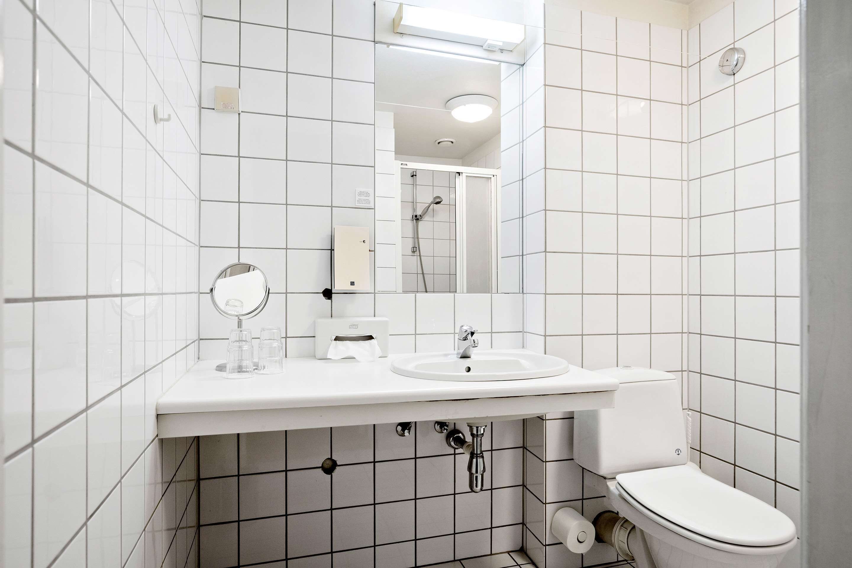 A modern bathroom with white tiles, a sink, a toilet, a mirror, and a shower.