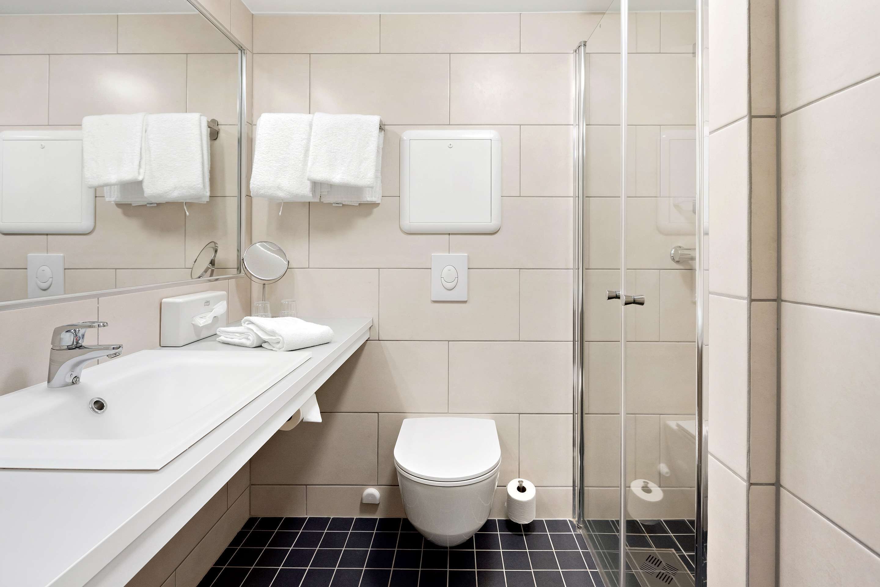 Un bagno moderno con un lavandino bianco, un WC, un box doccia in vetro e uno specchio.