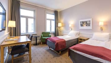 Quarto de hotel com duas camas, uma escrivaninha, uma cadeira, uma mesa pequena e duas luminárias.