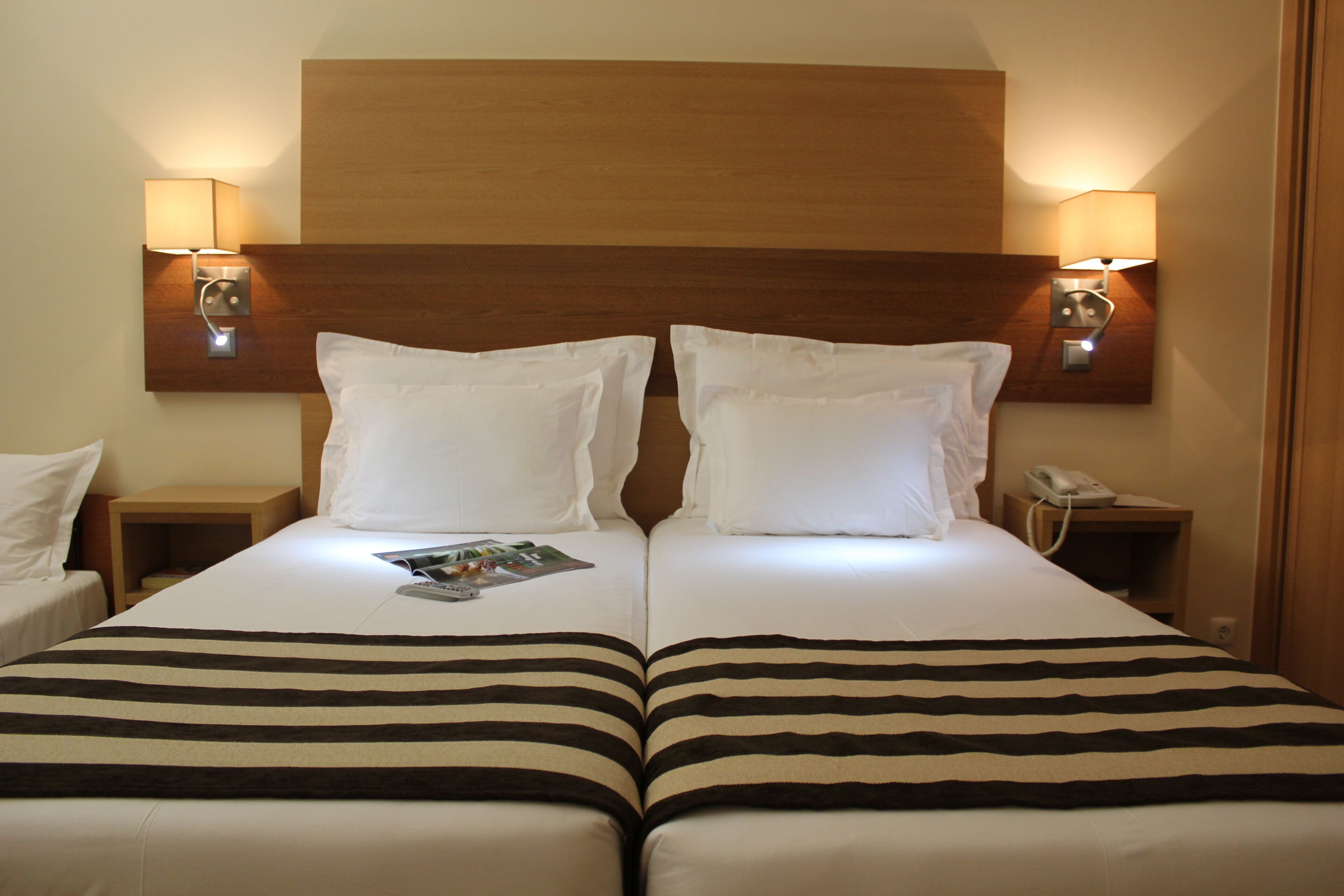 A double bed with striped bedding, two bedside lamps, a magazine, and a phone on the nightstand.