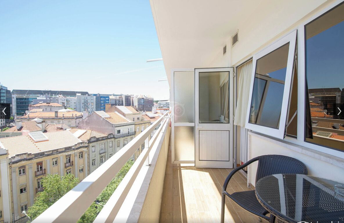 A balcony with a view of city buildings, a chair, and a table.