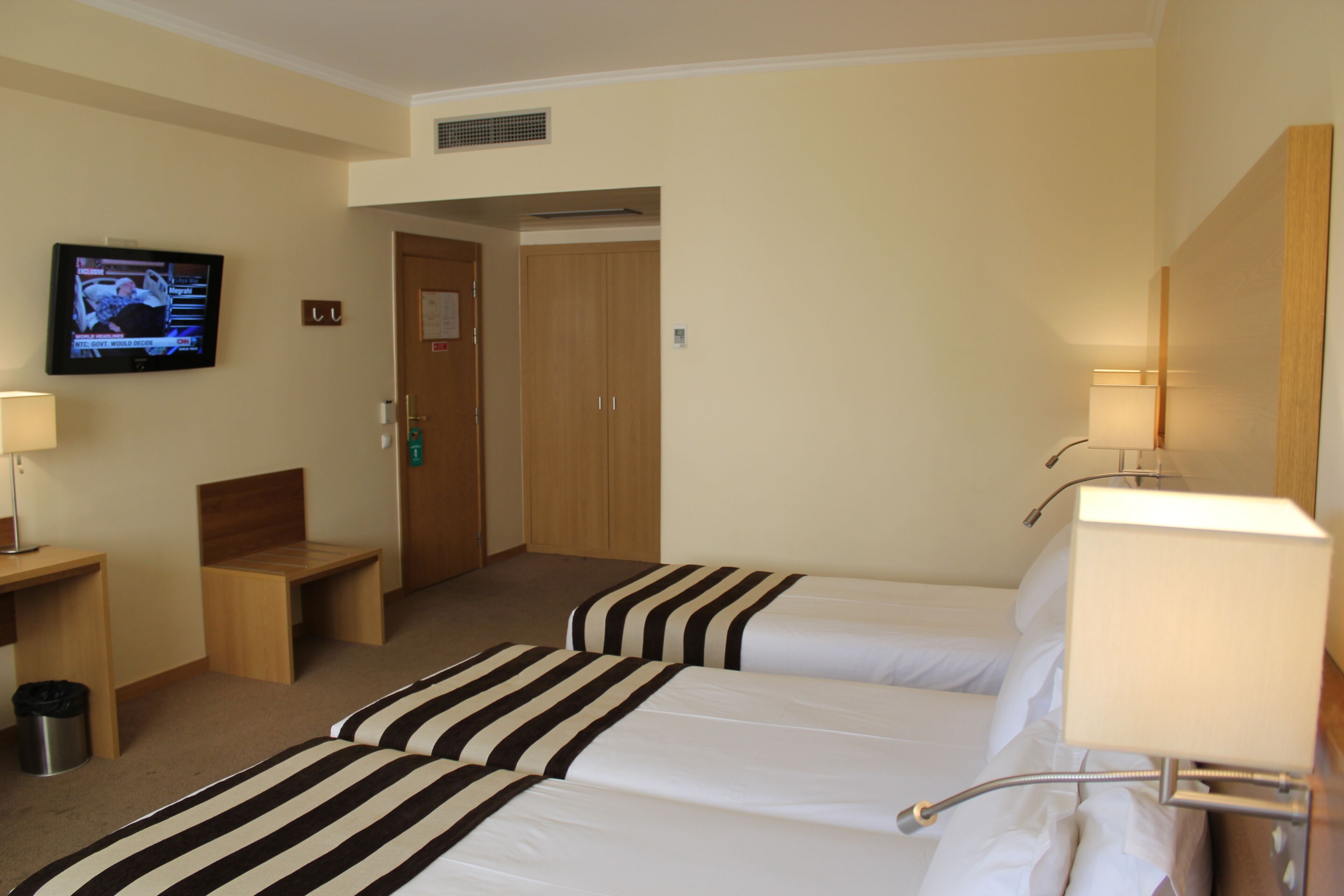 Une chambre d’hôtel avec deux lits, un téléviseur fixé au mur, un bureau et une poubelle.