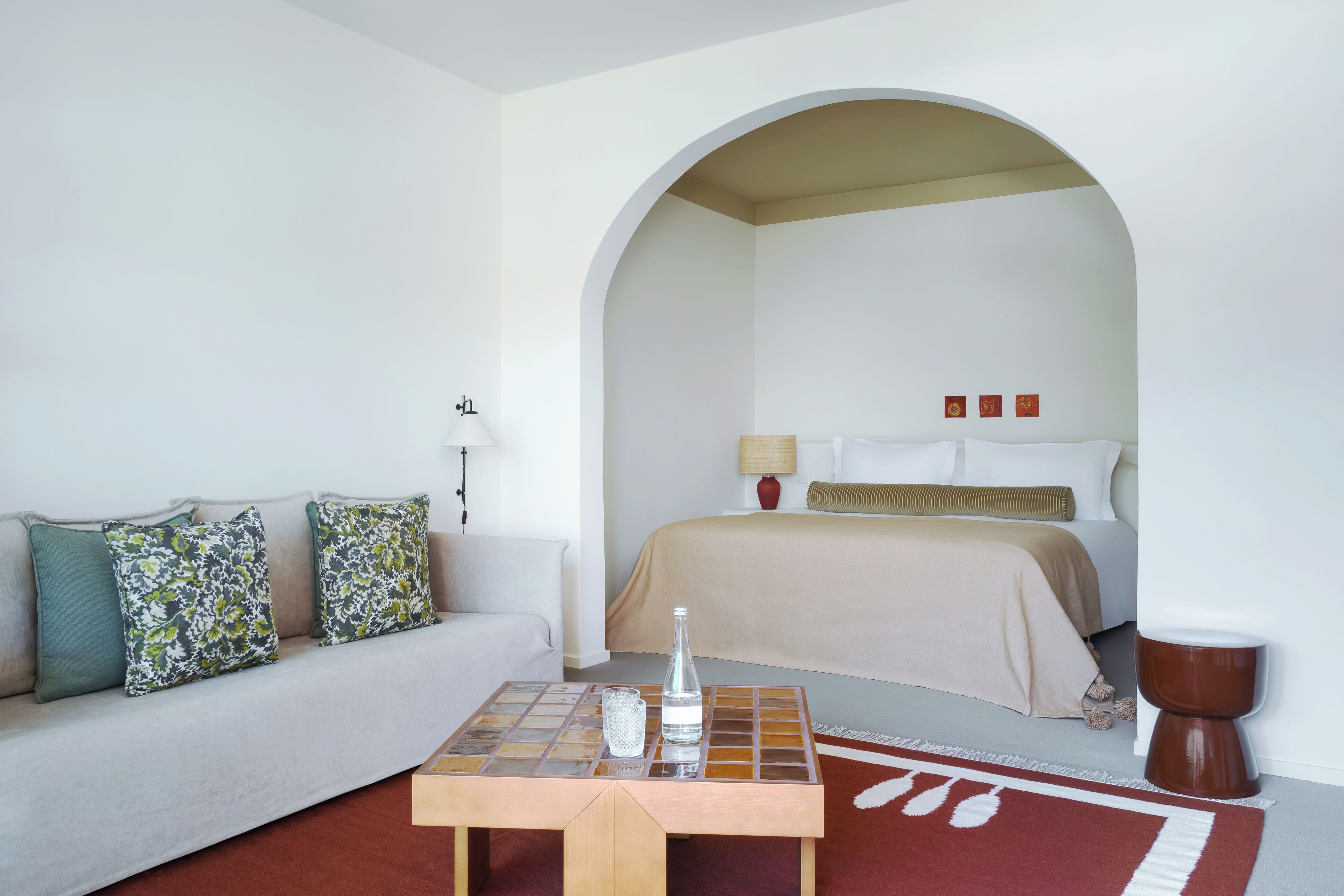 Ein Hotelzimmer mit einer Couch, einem Tisch mit Flasche und Glas, einem Bett mit beige farbenem Bettbezug und einer braunen Toilette.
