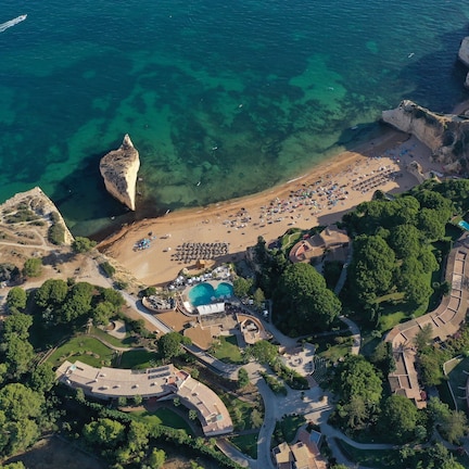 An aerial view of a coastal resort with a beach, swimming pool, and landscaped gardens.