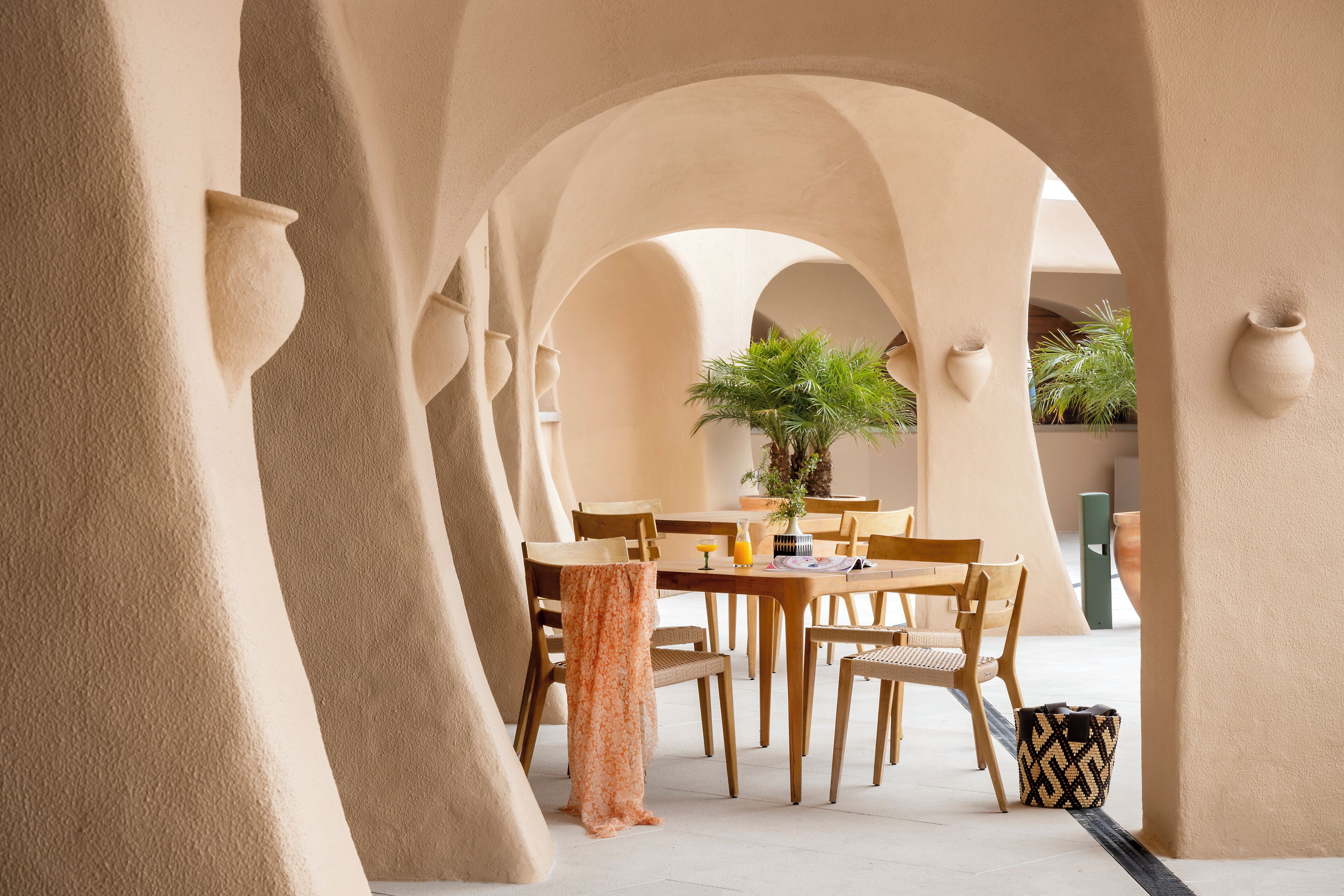 Un espace de restauration intérieur avec une table dressée pour quatre personnes, entourée de chaises en bois, sous une série d’arches.