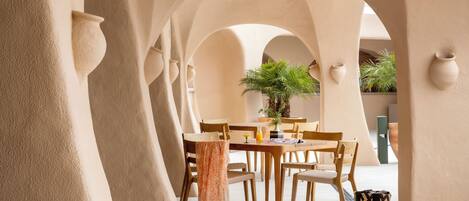 Un espace de restauration intérieur avec une table dressée pour quatre personnes, entourée de chaises en bois, sous une série d’arches.