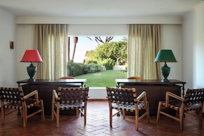A room with a view of a garden, a desk with two chairs, and two lamps.