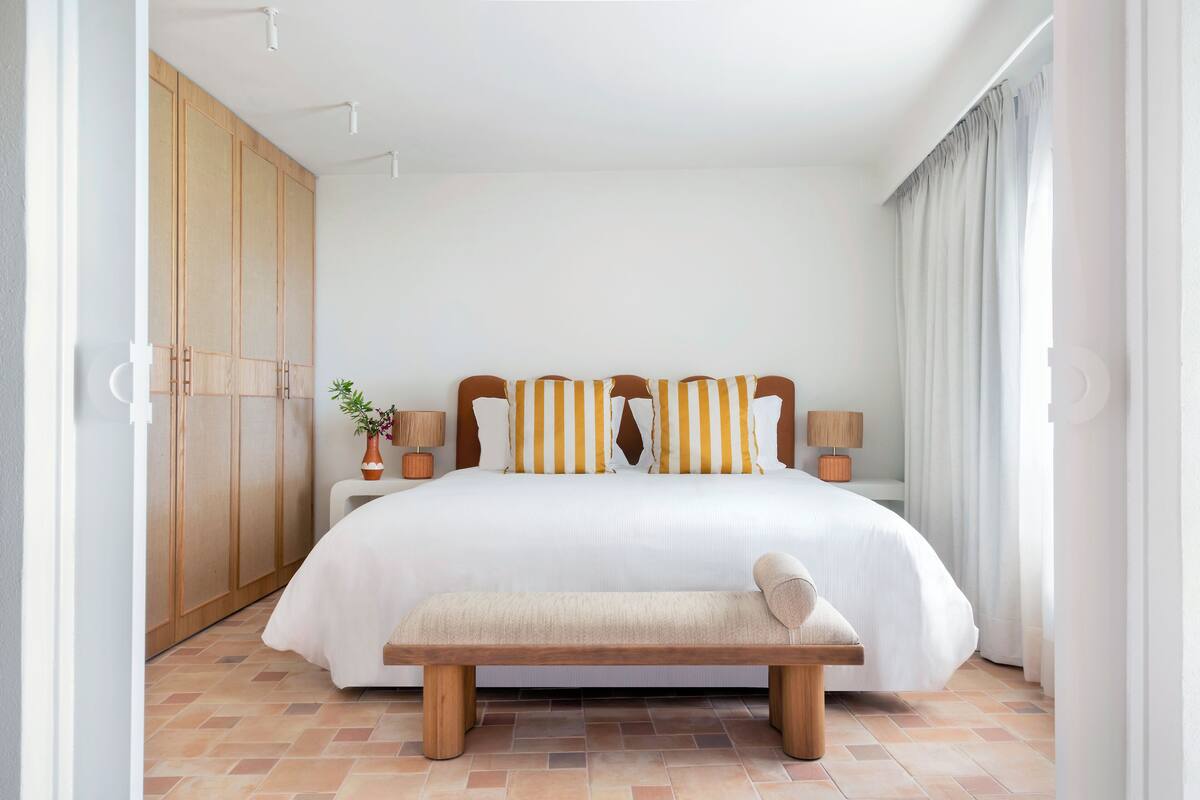 A spacious bedroom with a large bed, wooden wardrobe, bedside lamps, and a bench.