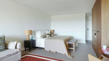 A hotel room with a bed, bedside tables, a chair, a small table, and a door.
