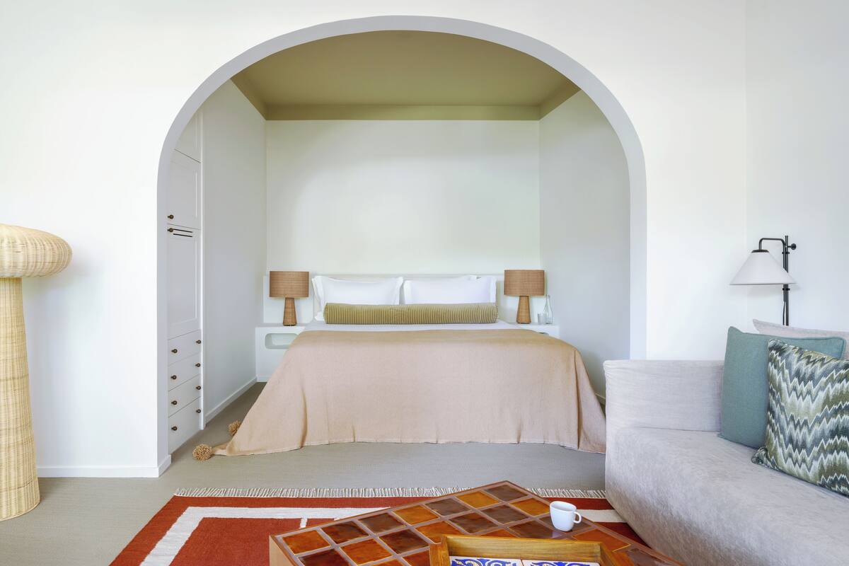 A bedroom with a bed, a sofa, a coffee table, and a lamp.