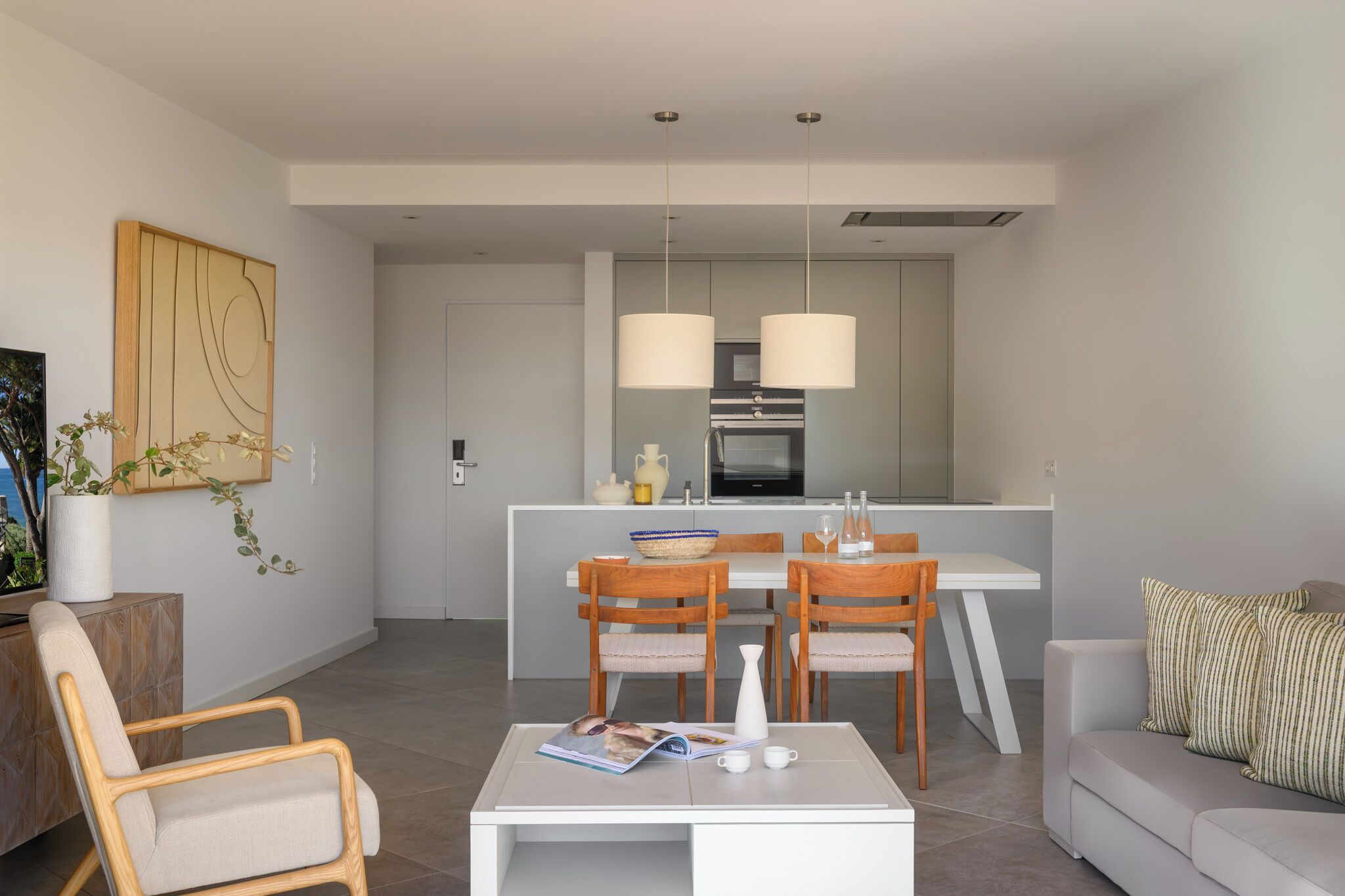 Una sala de estar moderna con un sofá, una mesa de centro y dos sillas de madera. Hay un comedor con una mesa y sillas, y una cocina al fondo.