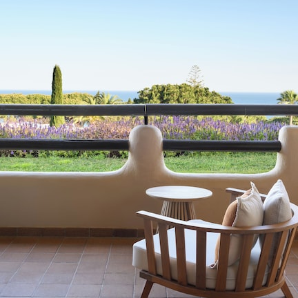 A balcony with a view of the sea, a chair with cushions, and a small table.