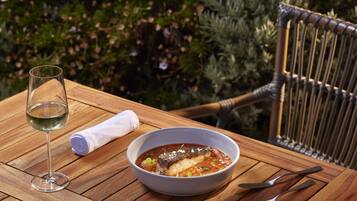 Una mesa de madera con un tazón de sopa y una copa de vino blanco, una servilleta doblada y cubiertos.