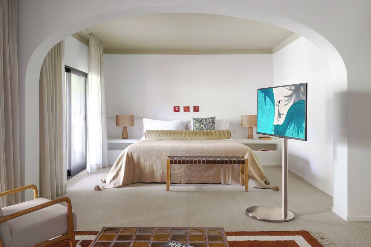 A modern hotel room with a large bed, a flat-screen TV, a bench, and a small table.