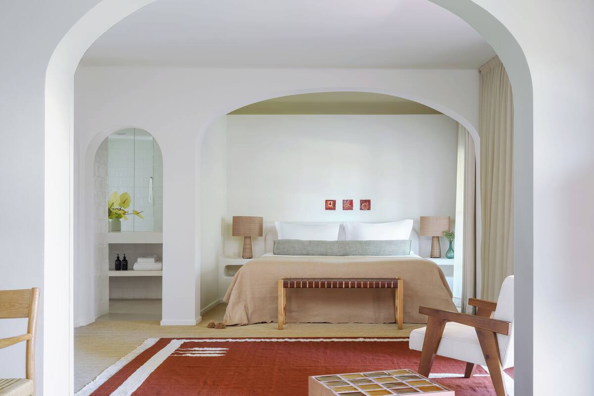 A bedroom with a large bed, two bedside tables, a bench, a chair, and a mirror.