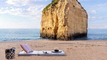 Ein Strand mit einer großen Felsformation, einer Liege und einer Tasche voller Bücher.