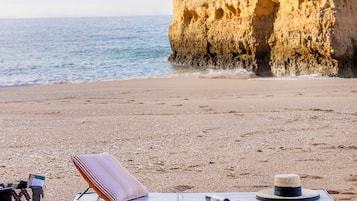 A beach with a cliff, a towel, a hat, and a bag on the sand.