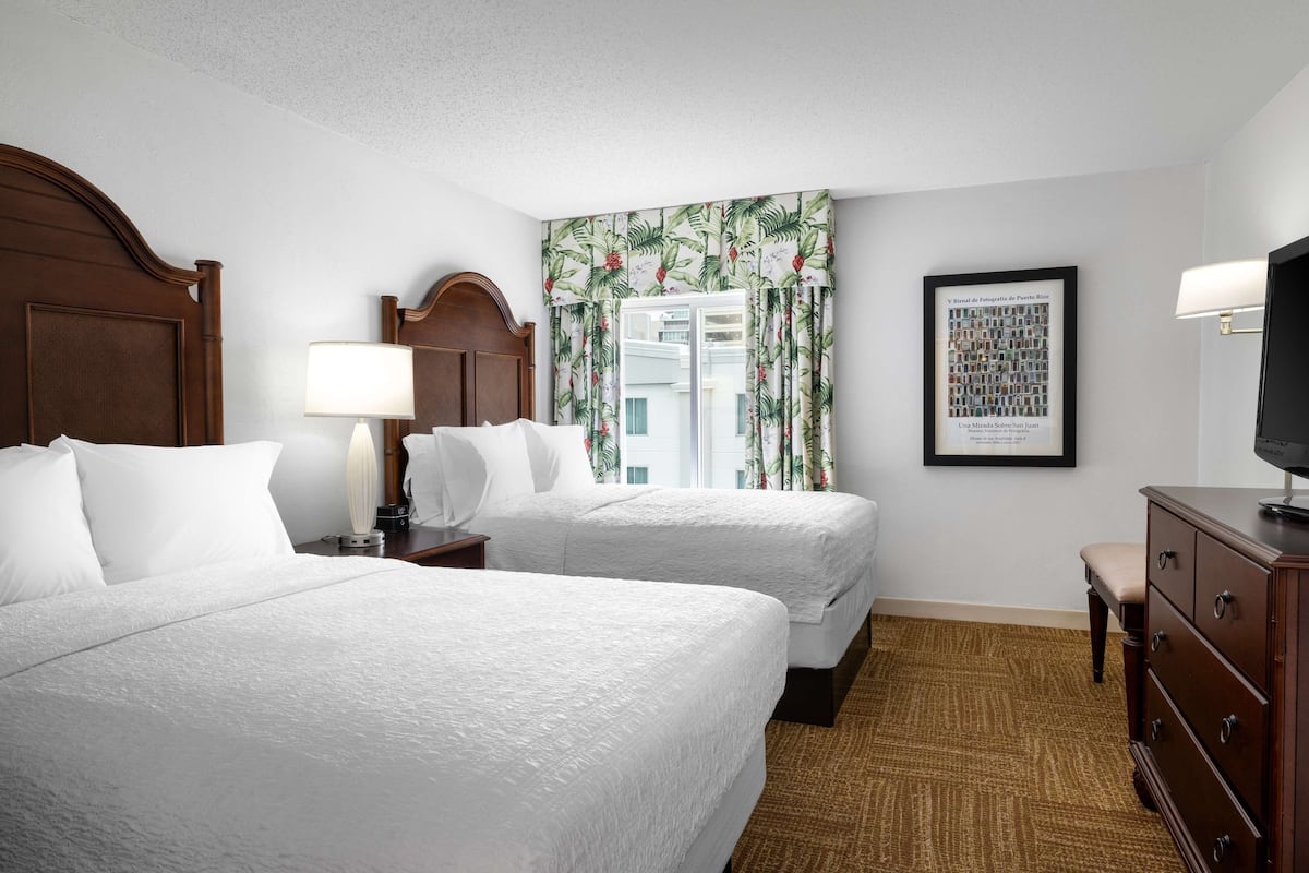 A hotel room with two beds, a nightstand with a lamp, a dresser, and a framed picture on the wall.