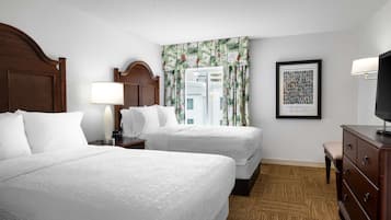 Habitación de hotel con dos camas, una mesita de noche con lámpara, un aparador y un cuadro en la pared.