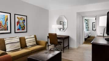 A modern hotel room with a sofa, a desk, a chair, a TV, and artwork on the walls.